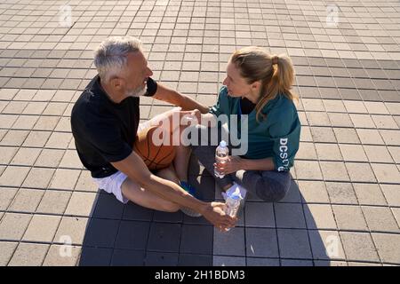 High angle view of mature couple in sportswear having a conversation while drinking water, relaxing outdoors on a sunny summer day Stock Photo