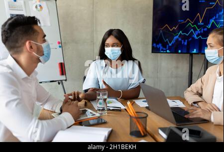 Business People In Medical Masks Having Discussion During Corporate Meeting In Office Stock Photo