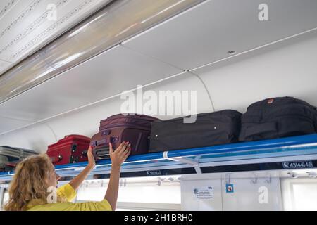 Female hands take off hand luggage. Young woman putting the baggage on the shelf in the train Stock Photo