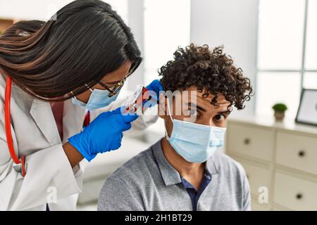 Young latin doctor woman auscultating the ear of man using otoscope at examination room. Stock Photo