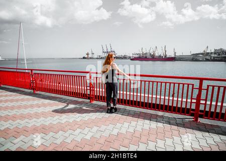 A girl is standing on the pier at the maritime station, waiting for the liner. Stock Photo