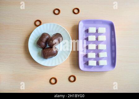 A purple plate with ten pieces of white sugar and a white plate with three chocolates are on the table. Top view Stock Photo