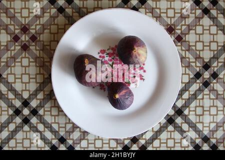 Three whole ripe juicy purple figs and on a white round plate Stock Photo