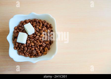 A plate with a bunch of coffee beans and two pieces of white sugar is on the table. Top view. Copy space. Assimilate concept. Stock Photo