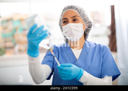 Female nurse wearing a protective mask fills a syringe with saline solution in the treatment room Stock Photo