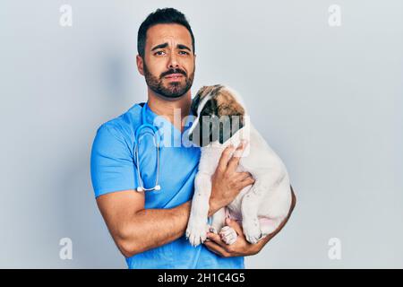 Handsome hispanic veterinary man with beard checking dog health clueless and confused expression. doubt concept. Stock Photo