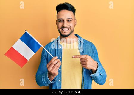 Young arab man holding france flag smiling happy pointing with hand and finger Stock Photo