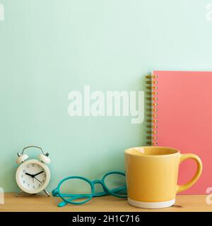 Notebook, mug cup, glasses, clock on wooden desk. mint wall background. workspace Stock Photo