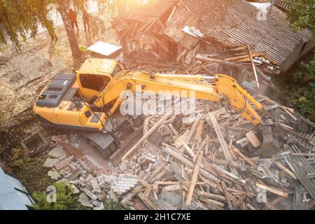 Excavator breaks old house, many dust in air. Building demolition and deconstruction, aerial view. Stock Photo