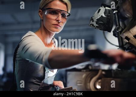 Portrait of mid adult industrial woman working indoors in metal workshop. Stock Photo