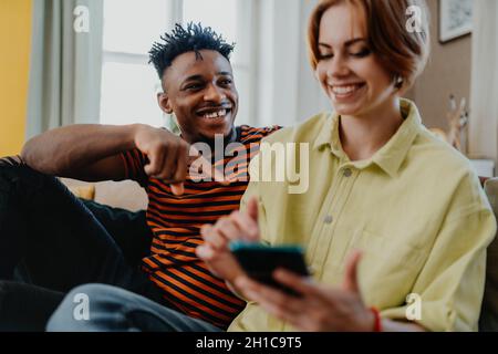 Young biracial couple using smartphone, having fun at home, checking social networks together. Stock Photo