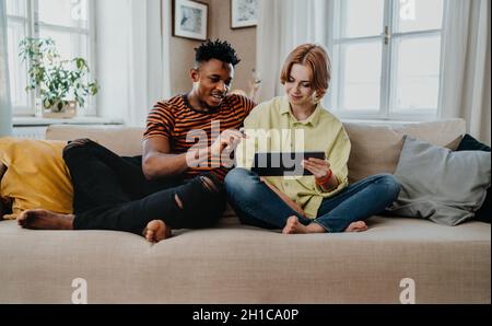 Young biracial couple using tablet, having fun indoors at home, checking social networks together. Stock Photo