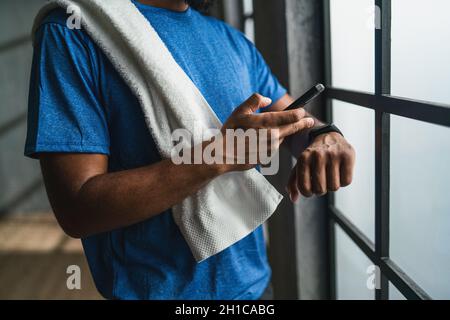 Unrecognizable young African American sportsman standing at gym, using smartphone and smartwatch Stock Photo