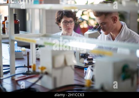 A young male chemistry student looking through a microscope in a laboratory in a relaxed atmosphere. Science, chemistry, lab, people Stock Photo