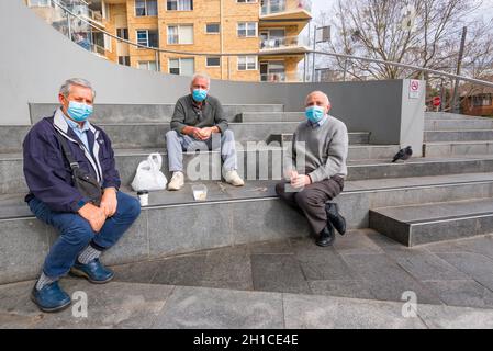 Three older men sitting separated but together on large concrete steps talking and drinking take-away coffee in Chatswood, Sydney, Australia Stock Photo