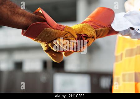 Two men engineers in workwear shaking hands against construction site. Stock Photo