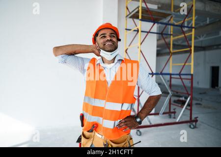 Portrait of mixed race man builder in workwear and hardhat wearing medical mask, close up Stock Photo