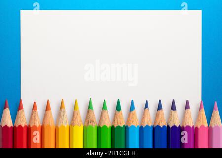 Frame made of color pencils and white paper on an blue background. Stock Photo
