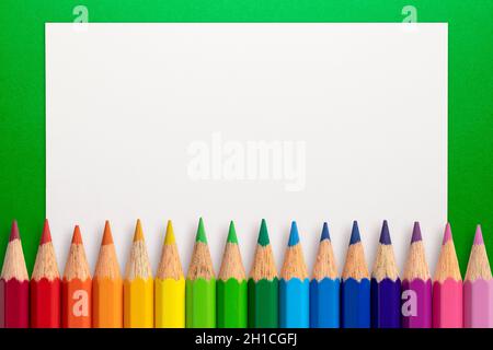 Frame made of color pencils and white paper on an green background. Stock Photo