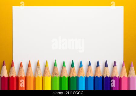 Frame made of color pencils and white paper on an yellow background. Stock Photo