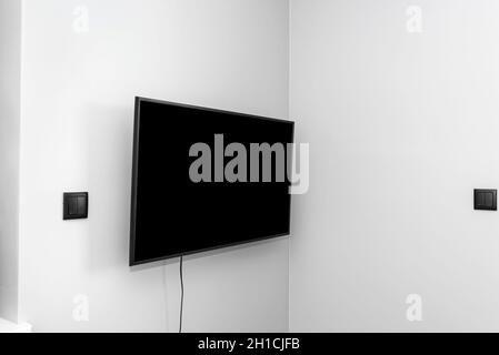 The TV is hung on the gray wall in the bedroom, the buttons for the blinds are visible. Stock Photo