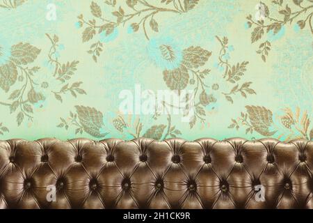 Retro styled image of an old chesterfield sofa in front of wallpaper with a floral pattern Stock Photo