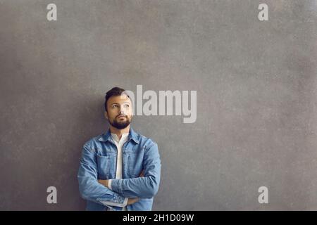 Handsome caucasian man with thinking expression standing on gray concrete background. Stock Photo