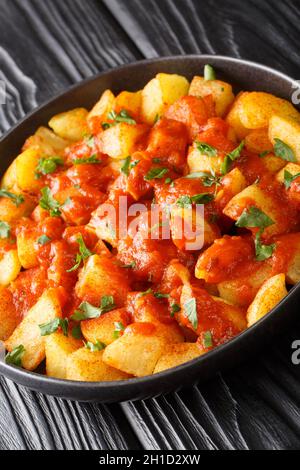 Patatas Bravas is a classic Spanish dish of fried potato cubes served with a spicy dipping sauce close up in the plate on the table. Vertical Stock Photo