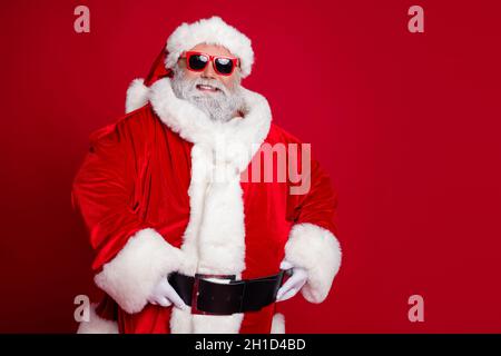 Photo of cheerful positive confident retired man hands belt wear santa hat costume isolated red color background Stock Photo