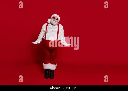 Photo of funny girlish adorable old man posing wear santa hat suspenders boots isolated red color background Stock Photo