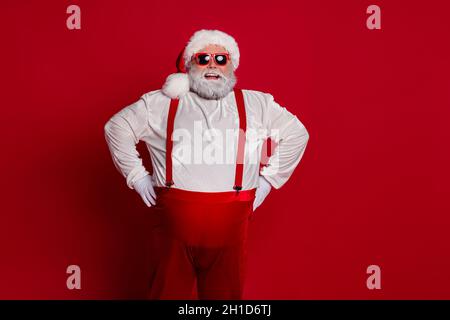 Photo of confident positive cheerful overweight man hands hips wear santa hat costume isolated red color background Stock Photo