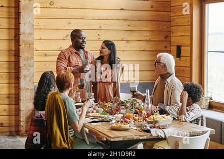 African young couple holding glasses with wine and saying the toast for their family at the table Stock Photo
