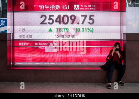 Hong Kong, China. 18th Oct, 2021. A woman sits next to a stock market display board showing the Hang Seng Index information (Photo by Miguel Candela/SOPA Images/Sipa USA) Credit: Sipa USA/Alamy Live News Stock Photo