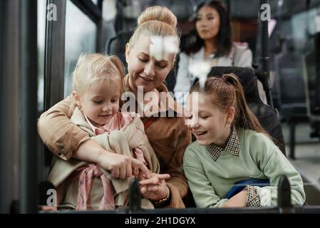 Portrait of adult woman with two kids having fun on bus while traveling by public transport in city Stock Photo