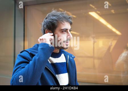 Handsome young man, putting on wireless earphones while walking, urban city background . Stock Photo