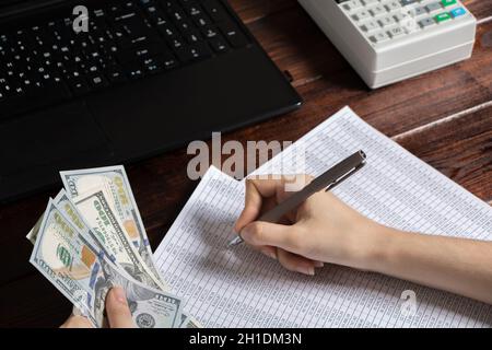 Obligation to pay wages and debts in the company.A cashier holds money dollars over an office work space with documents, a cash register, a phone, and