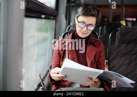 Portrait of elegant mature woman reading book on bus while traveling by public transport in city, copy space Stock Photo