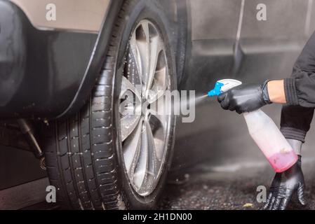 Professional car washer cleaning car alloy wheels . Stock Photo