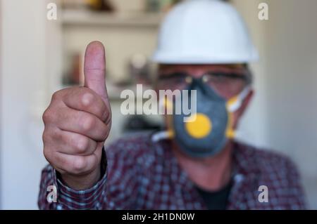 Worker shows thumbs up, with hard hat, safety glasses and protective mask, selective focus. Stock Photo