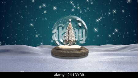 Snow falling over Christmas tree inside snow globe against green background Stock Photo