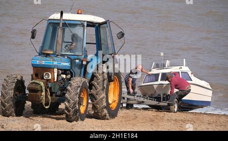 Pulling a fishing boat from the sea onto tractor drawn trailer. Hornsea, East yorkshire, UK. Stock Photo