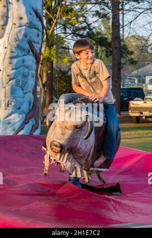 Young boy riding a mechanical bull at the Pine Hills Festival street fair in Stone County, Mississippi Stock Photo