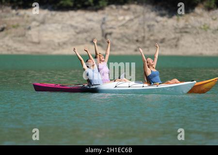 Three excited friends raisng arms celebrating vacation in a kayak in a beautiful lake Stock Photo