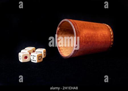 Leather dice cup with five poker dice on a black mat Stock Photo