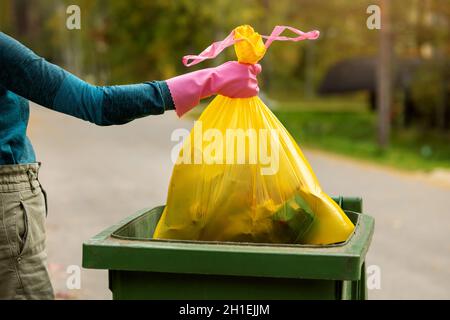 hand put a yellow plastic unsorted garbage bag into trash bin. household waste Stock Photo