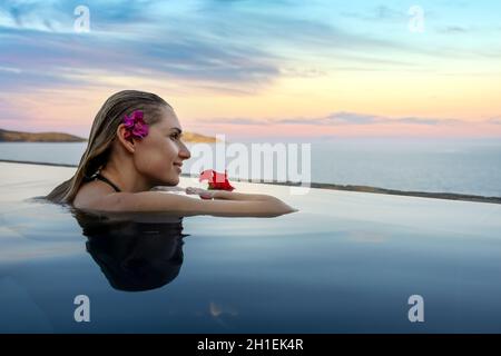 luxury resort vacation - woman with flower in the hair relaxing in infinity swimming pool with sea view. copy space Stock Photo