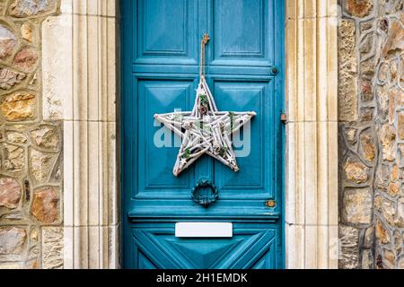 Front view of a star-shape Christmas decoration made of branches and pine cones, hanging on the blue front door with moldings of an old townhouse. Stock Photo