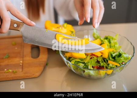 High-angle view of female hands putting chopped yellow bell peppers in fresh vegetarian vegetable salad, close-up. Stock Photo