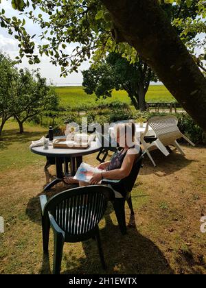 Woman making a lazy weekend morning at home in the garden with cup of coffee. Wear simple casual clothes and let the newspaper relax. Stock Photo