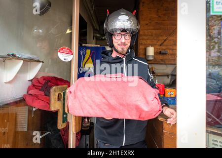 27/04/2020, lyon, Rhone Alpes Auvergne : Photo of happy man from delivery service in red t-shirt and cap giving food order and holding two pizza boxes Stock Photo